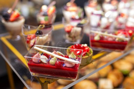 Un assortiment de desserts délicieux comprenant des mousses, des tartes et des gâteaux magnifiquement disposés sur une table en verre, tentant pour les papilles gustatives.
