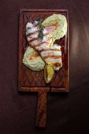 A delicious and healthy meal of grilled fish fillet with lemon and herb butter, served on a wooden board.