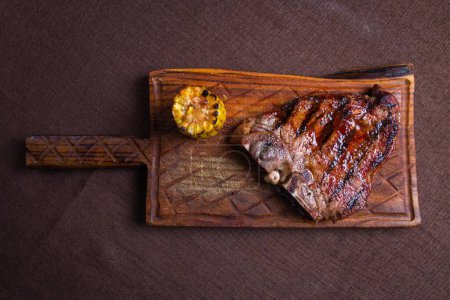 Téléchargez les photos : Un steak grillé juteux et tendre avec un côté de maïs sur l'épi, servi sur une planche à découper rustique en bois. - en image libre de droit