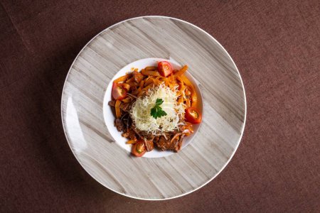 Vista superior de un delicioso plato de estofado de ternera con pasta, tomates y queso, perfecto para el almuerzo o la cena.
