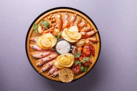 Un plato de mariscos delicioso y fresco con varios tipos de camarones, cuñas de limón y papas fritas, servido en una tabla de madera.