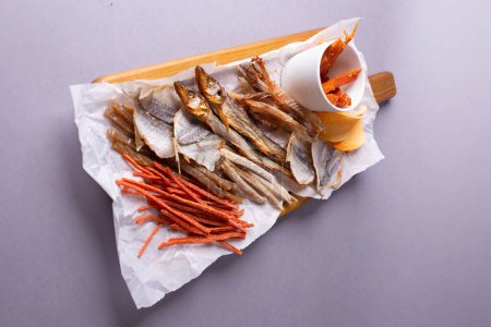Eine Vielzahl von dehydriertem Fisch, Möhren und Kürbisscheiben auf weißem Papier vor grauem Hintergrund. Isoliert auf grauem Hintergrund.