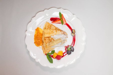 Isolated image of a gourmet pancake on a white plate with red sauce and berries, perfect for food blogs or recipe websites.