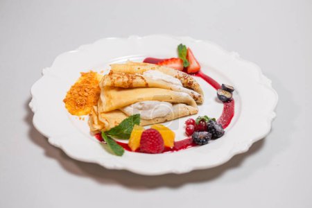 A decadent plate of crepes filled with a sweet and creamy cheese filling and topped with fresh strawberries, blueberries, and red currant.