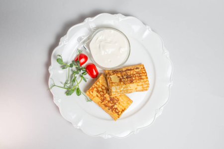 Top view of Pancakes with sour cream and cherry tomatoes on a white background. Carnival menu.
