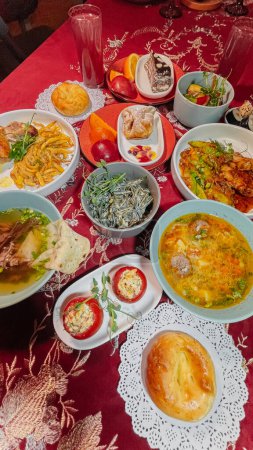 Top view of Uzbek traditional dishes on a table with red tablecloth. Soups, salads, main courses, pastries, drinks.