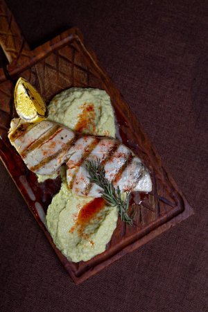 A delicious and healthy meal of grilled fish fillet with lemon and herb butter, served on a wooden board.
