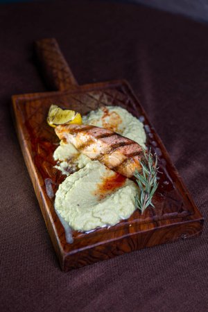 A mouthwatering grilled salmon fillet topped with a zesty lemon-herb butter sauce, presented elegantly on a rustic wooden serving board.