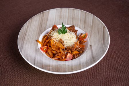 Top view of a delicious plate of beef stew with pasta, tomatoes, and cheese topping, perfect for lunch or dinner.
