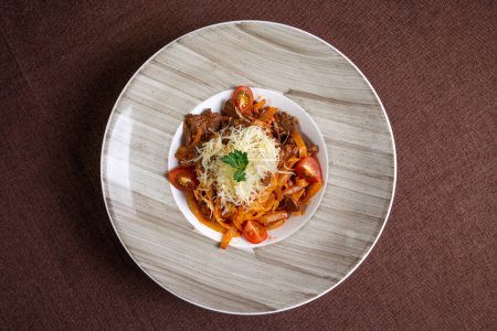Blick von oben auf einen köstlichen Teller Rindereintopf mit Nudeln, Tomaten und Käsebelag, perfekt zum Mittag- oder Abendessen.