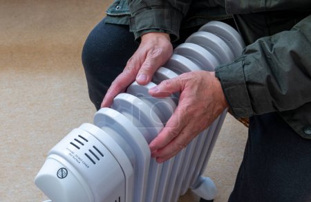 A person sitting in a room hugging a portable electric heater trying to keep warm in the Winter cold.