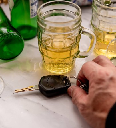 Téléchargez les photos : Un concept de conduite avec une table pleine de boissons alcoolisées et une personne ramassant un ensemble de clés de voiture pour conduire. - en image libre de droit