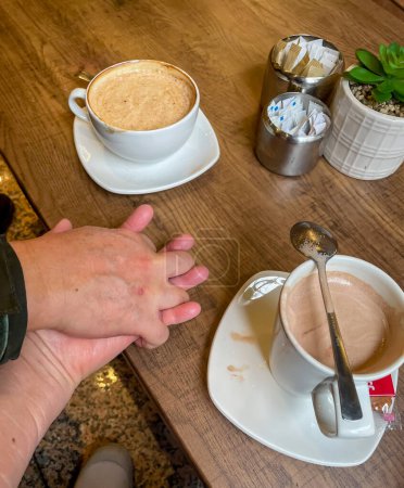 A couple holding hands while enjoying hot drinks.