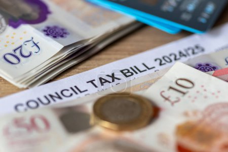 Gros plan sur un projet de loi d'impôt du Conseil des autorités locales du Royaume-Uni avec billets de banque, pièces de monnaie et cartes bancaires.