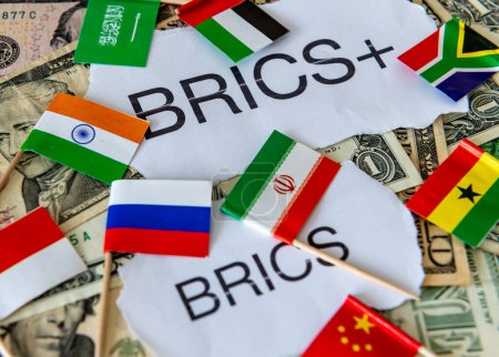 The words and country flags of some of the BRICS and BRICS+ block of countries on top of a pile of US dollar bills. A dedollarisation concept.