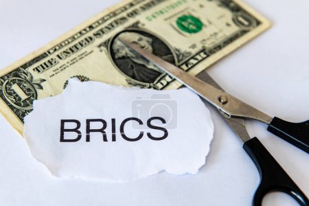 A dedollarisation concept with a dollar bank note, the word BRICS and a pair of scissors isolated in white.
