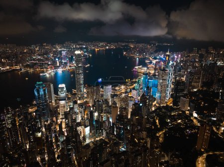 Téléchargez les photos : Au-dessus du paysage urbain nuageux de l'île de Hong Kong, vue de nuit aérienne par drone. Bâtiments de gratte-ciel dans le quartier financier, transport maritime sur le port de Victoria. Asie tourisme concept de voyage - en image libre de droit