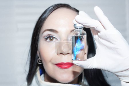 Photo for Doctor of biomolecular medicine scientist holds between her fingers a vial containing the double helix DNA elicitor with RNA copy human genetic copy vaccine - Royalty Free Image