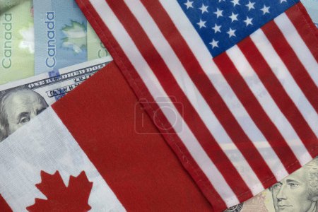 United States and Canadian flags on US dollar and Canadian loonie currencies. Flat lay. Concept of vacation, trade, finance, travel, currency exchange and business cooperation. Macro close up