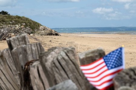 Utah Beach WWII mit Flagge der USA mit selektivem Fokus auf Strand und Ozean. Sandstrand und Zaunpfähle. In der Normandie erinnert Frankreich an den Veteranentag. Hochwertiges Foto