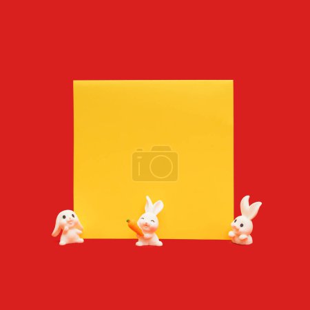 Téléchargez les photos : Lapins mignons avec une maquette de carte de papier d'invitation carrée jaune sur fond rouge vif. 2023. Nouvel An lunaire, composition de l'Année du lapin. - en image libre de droit