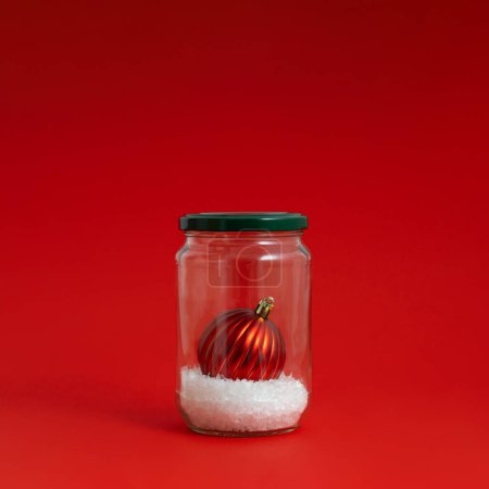 Téléchargez les photos : Boule de Noël rouge avec neige dans un bocal en verre. Fond d'hiver créatif. Couché plat, vue du dessus. - en image libre de droit