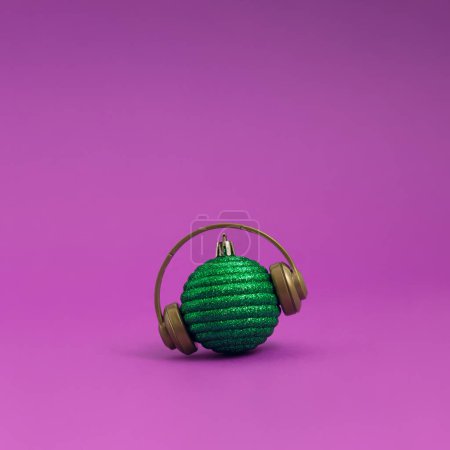 Foto de Bola de Navidad verde con auriculares sobre un vibrante fondo púrpura. Concepto de Navidad, Año Nuevo y vacaciones de invierno música y felicidad. - Imagen libre de derechos