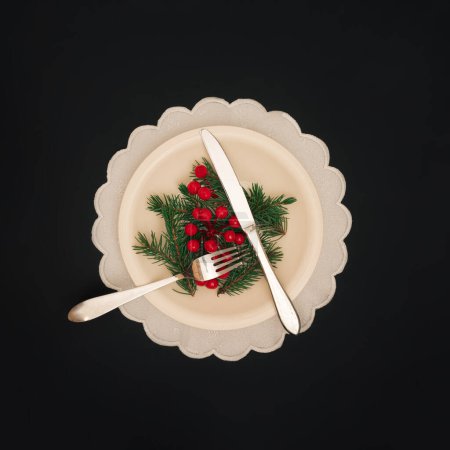 Christmas dinner concept. Silver cutlery, Christmas tree branches and red berries  over a black background. Christmas and New Year background.