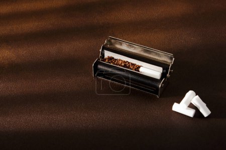 Photo for Hand-rolled cigarette, rolling machine, scattered tobacco on background, cigarette roll with filter, cigarette filters - Royalty Free Image