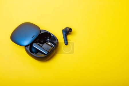 Téléchargez les photos : Blue wireless bluetooth earbuds or earphone with charging case on a yellow background. Colors of Ukraine. Possible social concept Hear the other. Copy space. - en image libre de droit