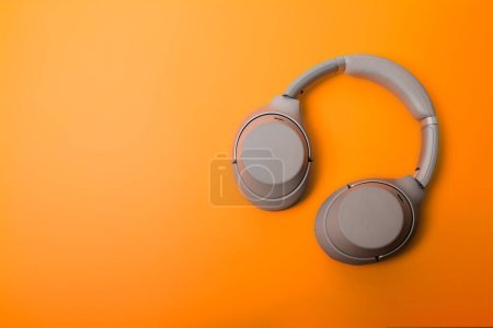 Light gray wireless over-ear headphones on an orange background. Headphones for playing games or listening to music. Noise canceling headphones. Top view. Copy space