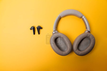 Téléchargez les photos : Light gray wireless on-ear headphones and blue in-ear wireless headphones on a yellow background. Comparison of different types of headphones. Headphones for playing games or listening to music. Noise canceling headphones. Top view. Copy space. - en image libre de droit