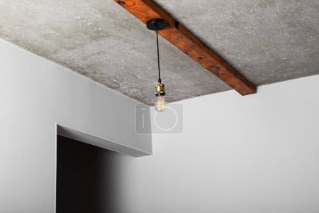 Loft style elements in the interior. Vintage incandescent light bulbs are spotted on wooden beams on a bare concrete ceiling