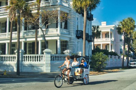 Foto de Charleston, Estados Unidos - 7 de noviembre de 2022: antiguas casas históricas con fachadas coloridas alrededor de pequeñas calles y ciclotaxi con gente en ella - Imagen libre de derechos