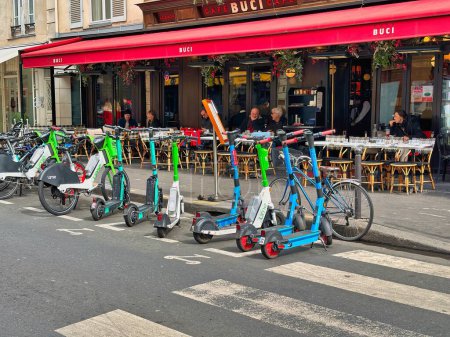 Téléchargez les photos : Paris, France - 11 avril 2023 : de petits scooters électriques sont stationnés sur la rue parisienne devant la terrasse d'un restaurant - en image libre de droit