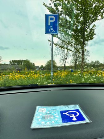 Photo for Capelle aan den IJssel, netherlands - May 06 2023: a handicaped parking card is displayed behind the front window of a car at a parking place with handicapped sign - Royalty Free Image