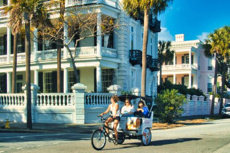 Foto de Charleston, Estados Unidos - 7 de noviembre de 2022: antiguas casas históricas con fachadas coloridas alrededor de pequeñas calles y ciclotaxi con gente en ella - Imagen libre de derechos