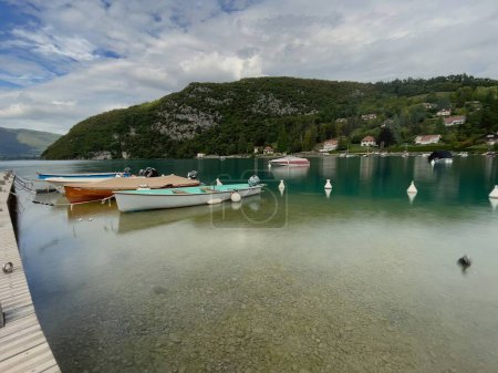 Foto de Talloires, francia - 15 de septiembre de 2022: barcos en bahía en el lago de montaña annecy con agua de color turquesa y montañas - Imagen libre de derechos