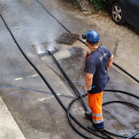 Foto de Menthon Saint Bernard, Francia - 09 de septiembre de 2021: un trabajador profesional está ocupado con un coche bomba y una manguera bajo alta presión limpiando un tubo de alcantarillado - Imagen libre de derechos