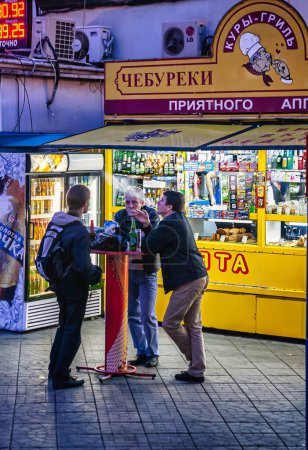 Photo for Moscow, Russia - September 10 2010 : men are standing around a table outside drinking and smoking infront of a street vending food and beverage store - Royalty Free Image