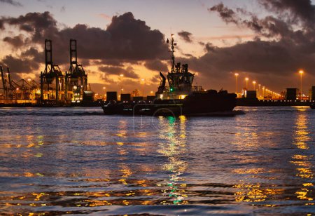 Foto de Rotterdam, Países Bajos - 11 de noviembre de 2021: un remolcador flota en las aguas superficiales de un puerto por la noche con reflexión sobre las luces - Imagen libre de derechos