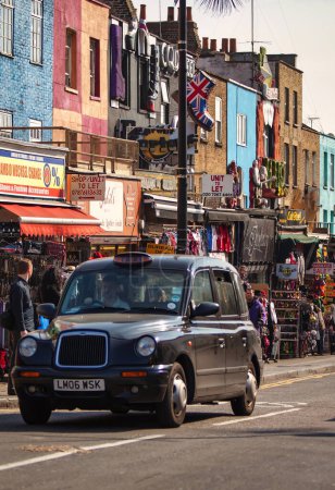 Photo for London, United Kingdom - March18 2009 : a classic london cab passes colorful camden road market - Royalty Free Image
