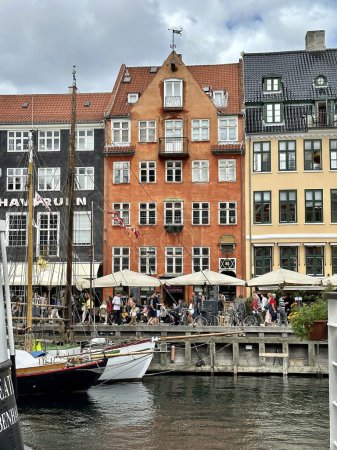 Téléchargez les photos : Copenhagen, Danemark - 24 juillet 2023 : les visiteurs se promènent dans le célèbre port de nyhavn avec des maisons colorées et des bateaux classiques amarrés dans l'eau - en image libre de droit