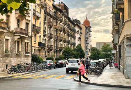 Foto de Ginebra, Suiza - 15 de septiembre de 2021: una persona está caminando en la acera cerca de un cruce con un típico edificio de apartamentos geneva clásico - Imagen libre de derechos