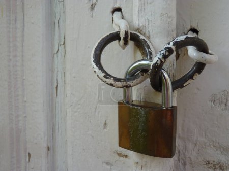 Rusty authentic padlock that keeps a white old vintage door locked