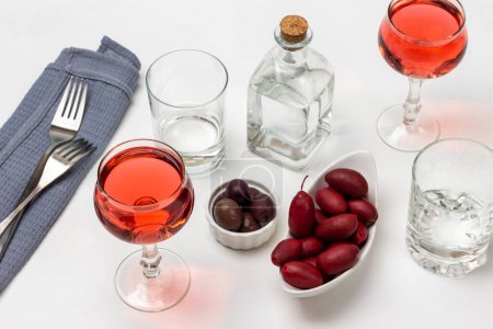 Foto de Two glasses of rose wine. Olives in a white plate. Empty glasses and a bottle of water. Two forks on a gray napkin. White background. - Imagen libre de derechos
