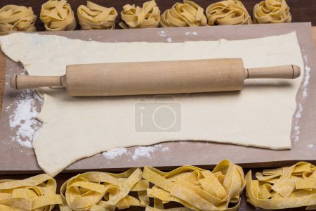 Process of making cooking homemade food. Rolling pin on rolled dough. Raw pasta on table. Wood backgroun