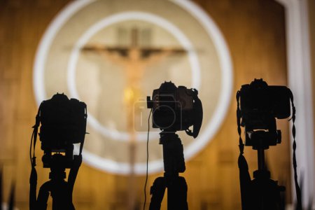 Cameras in front of a cross with the word jesus on it