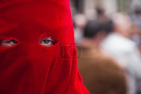 A penitent with a red scarf covering her eyes is seen in a street.