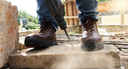 Téléchargez les photos : Un travailleur percait des roches et portait des chaussures de sécurité pour protéger ses pieds - en image libre de droit